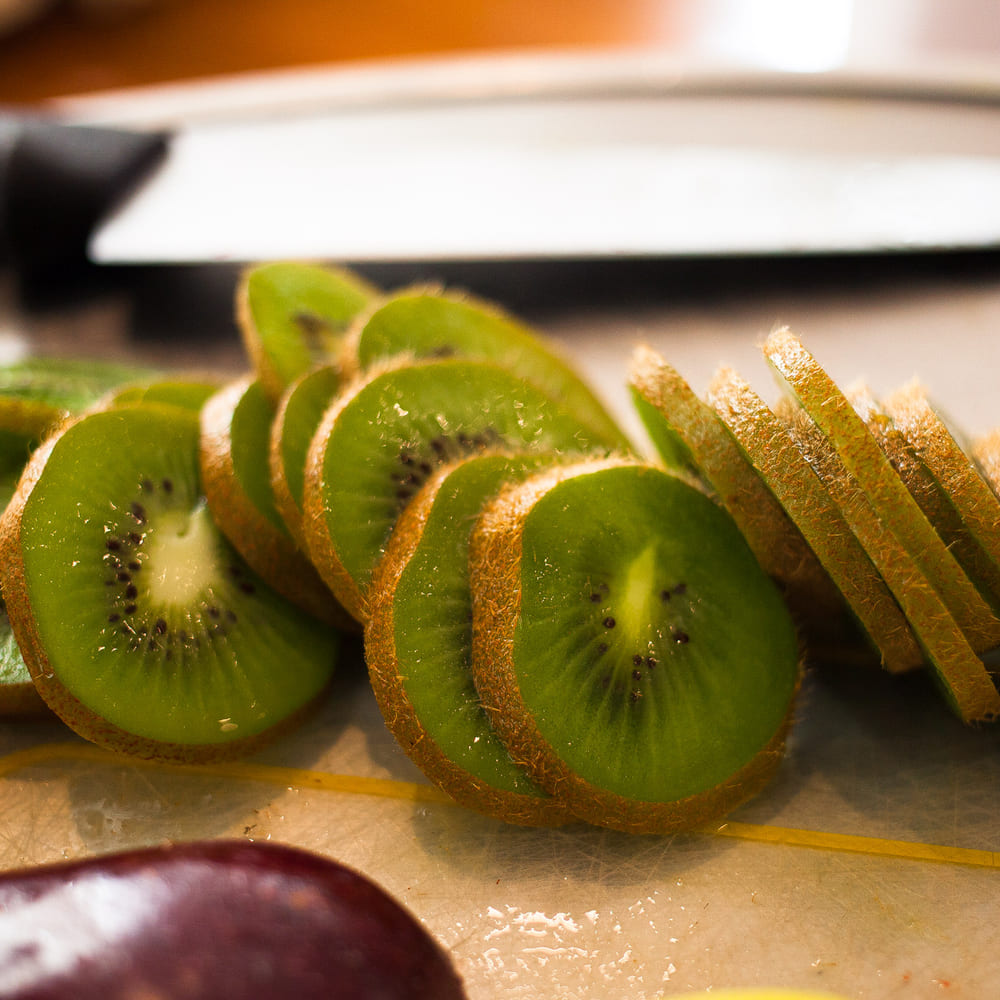 Kiwi sliced into rounds and batons on a wooden board beside a chef's knife.