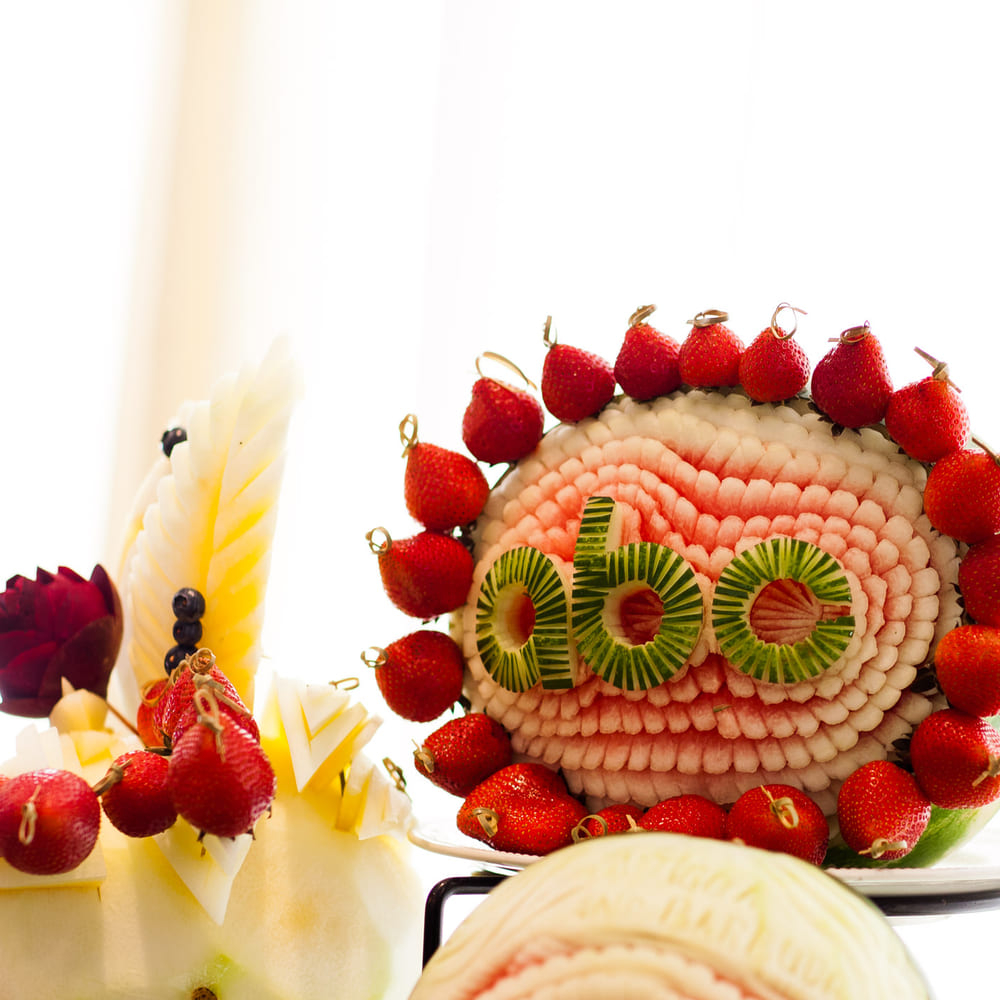 A carved watermelon ringed with strawberries on skewers, kiwi rounds set into the fluted white rind.