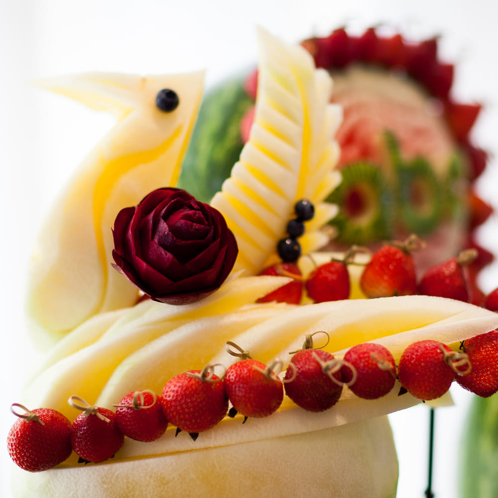 A swan carved from honeydew melon with a carved rose at its breast and strawberries on skewers.