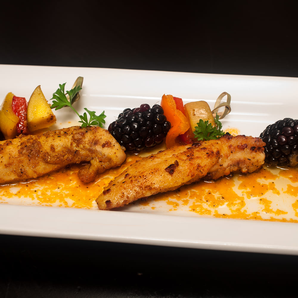 Seared chicken strips on a long white plate with blackberries, peach and pepper skewers and a saffron sauce.