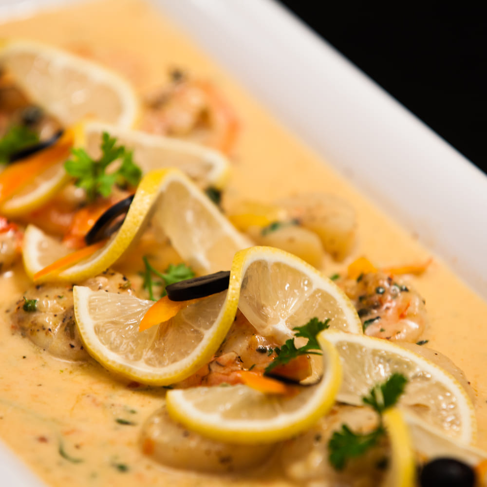 A tray of seafood in a saffron cream sauce with lemon slices, mussels, olives and parsley.