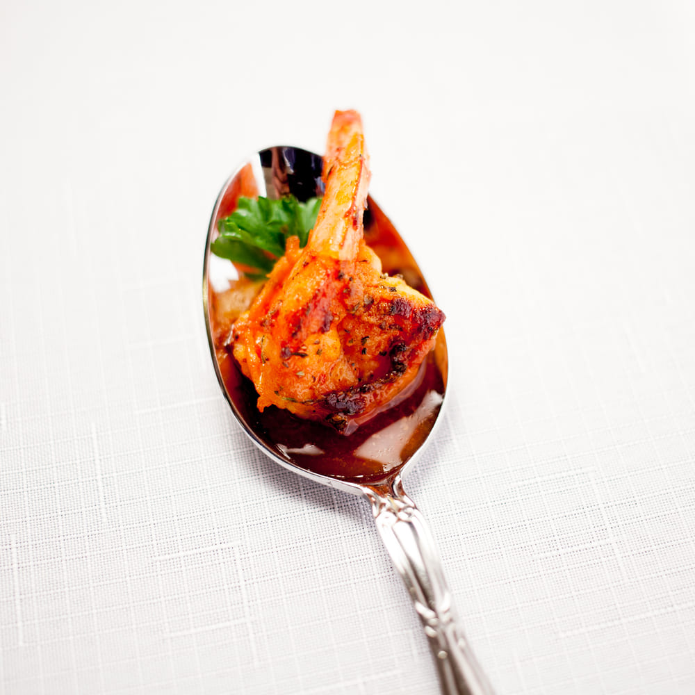 A single spiced prawn served on a silver spoon with parsley, on white linen.