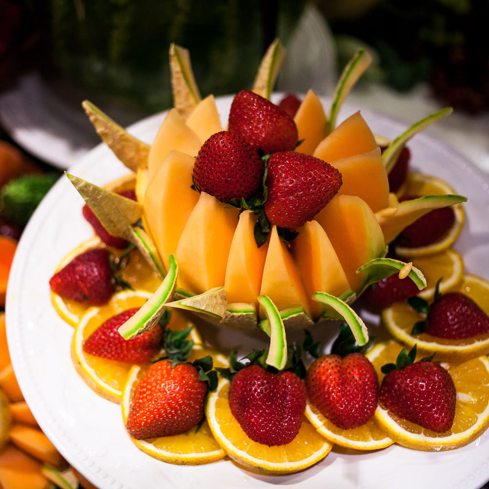A cantaloupe crown cut into petals and filled with strawberries, ringed with orange slices and lime.