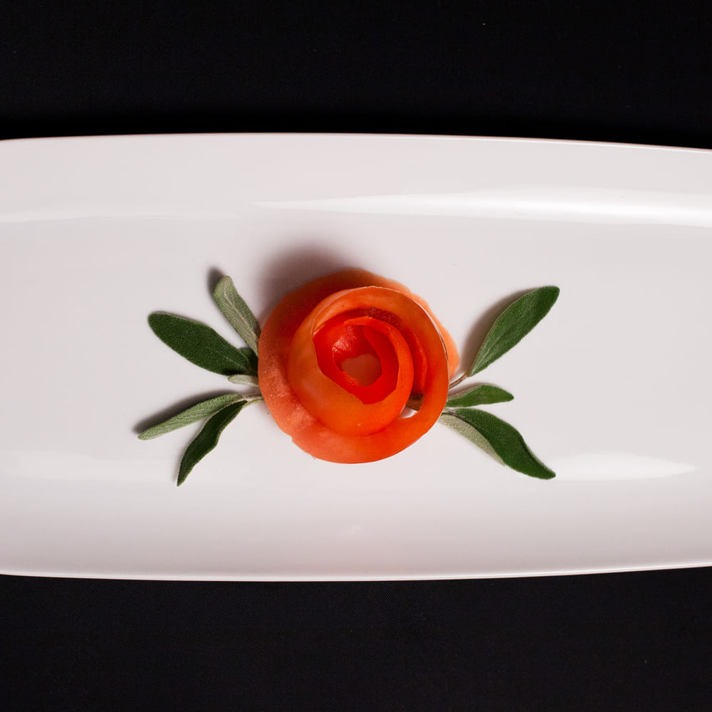 A single tomato rose with sage leaves, centred on a long white plate against black.