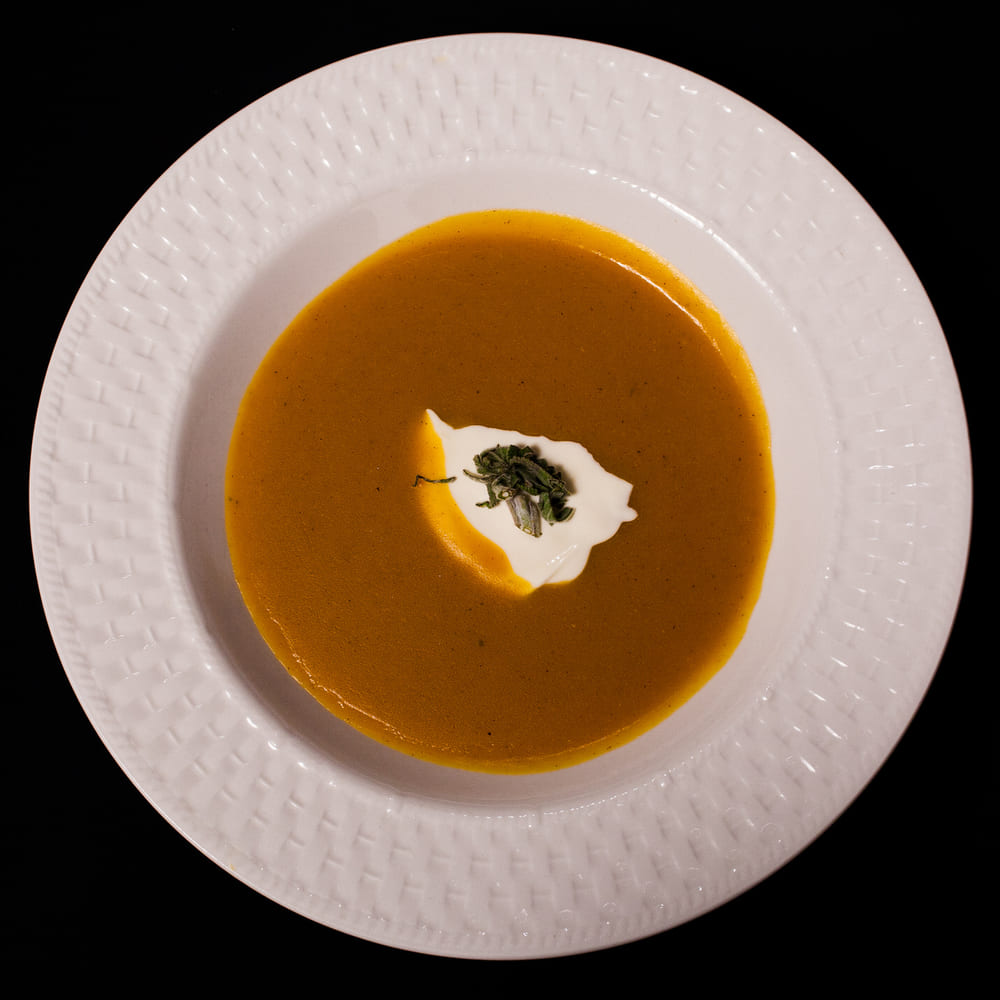 A bowl of smooth pumpkin soup with a quenelle of cream and herbs, shot from above on a white plate.