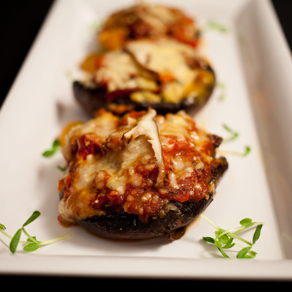 Stuffed portobello mushrooms with tomato and melted cheese on a white plate with micro herbs.