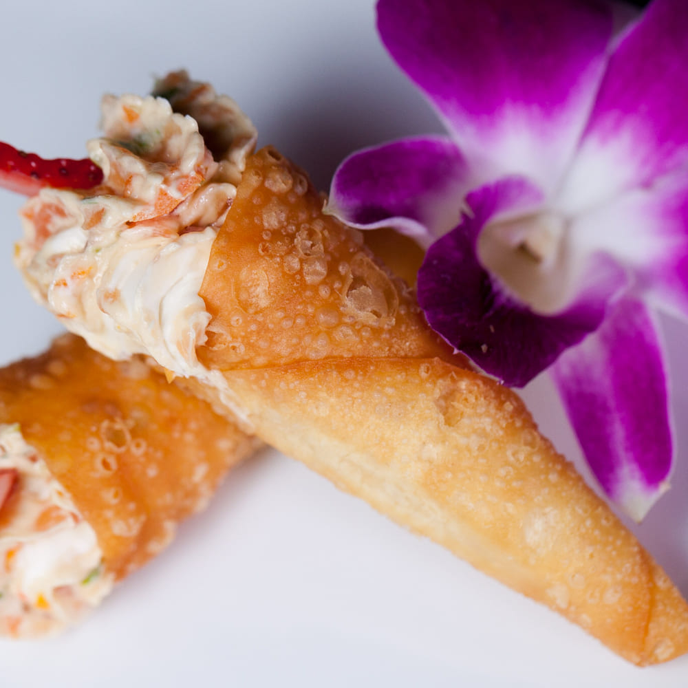 Two crisp pastry cones filled with a creamy seafood salad, garnished with a purple orchid.