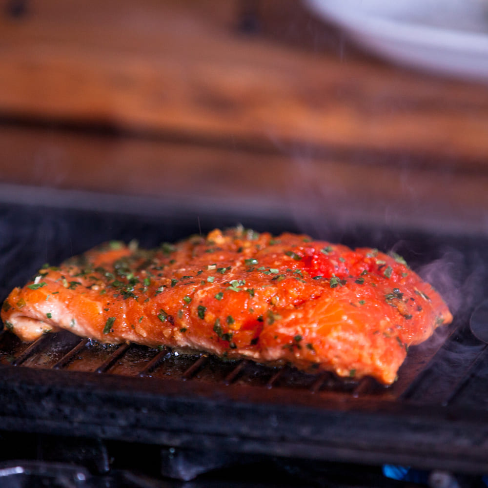 A salmon fillet in a spiced tomato glaze searing on a hot grill.