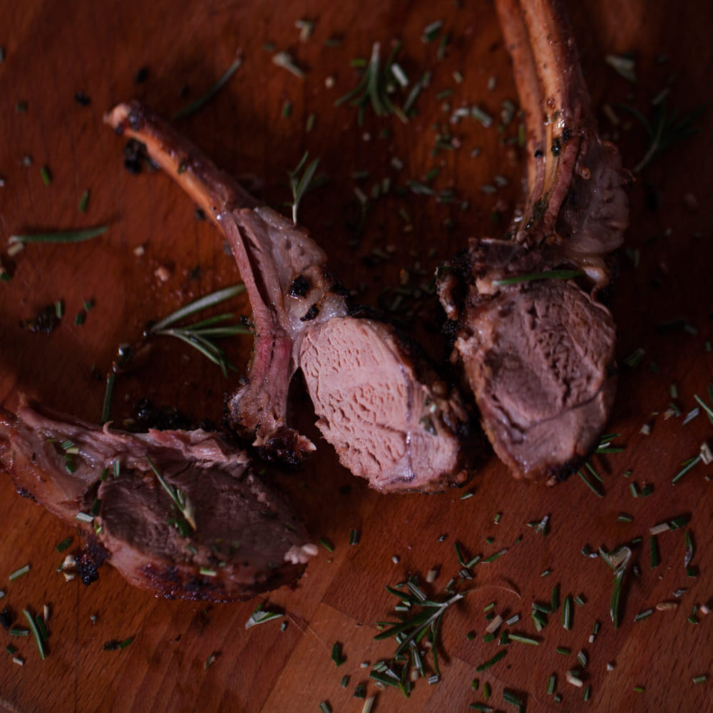 A rack of lamb carved into chops on a wooden board, scattered with rosemary.