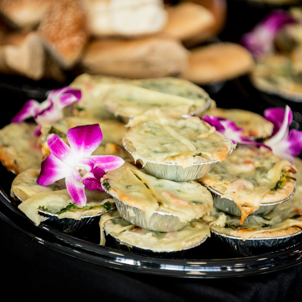 Mini spinach and cheese tarts with orchids on a black platter, croissants and pastries behind.