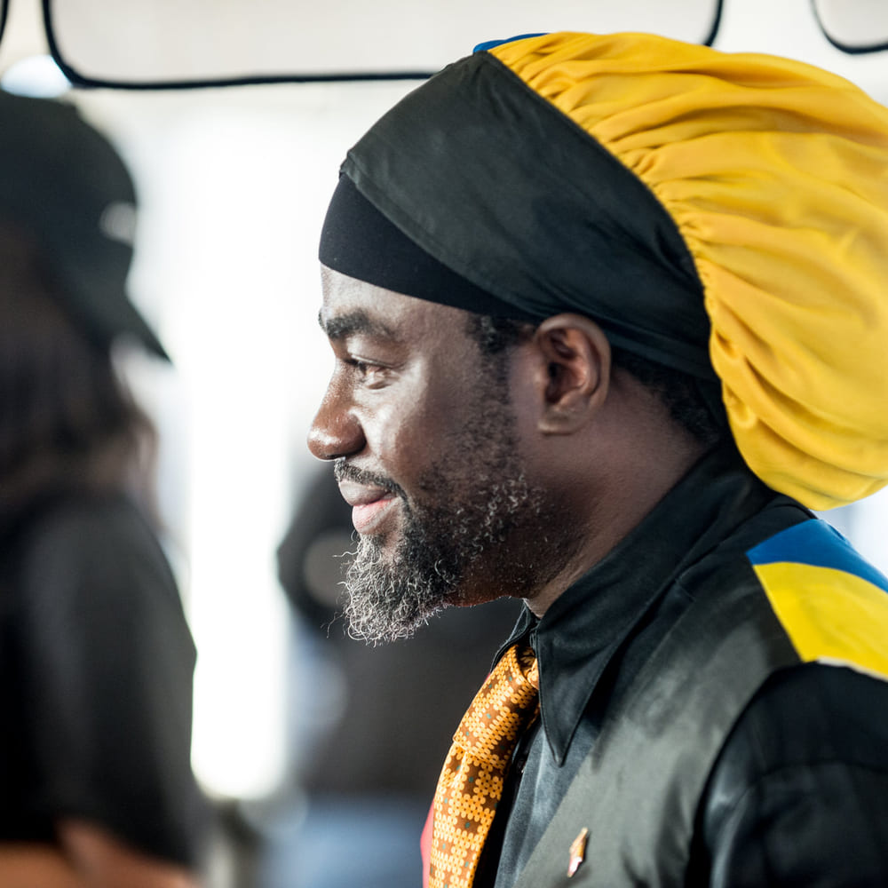 Chef Melvin Myers in profile wearing a black and yellow head wrap and an Antiguan flag sash.