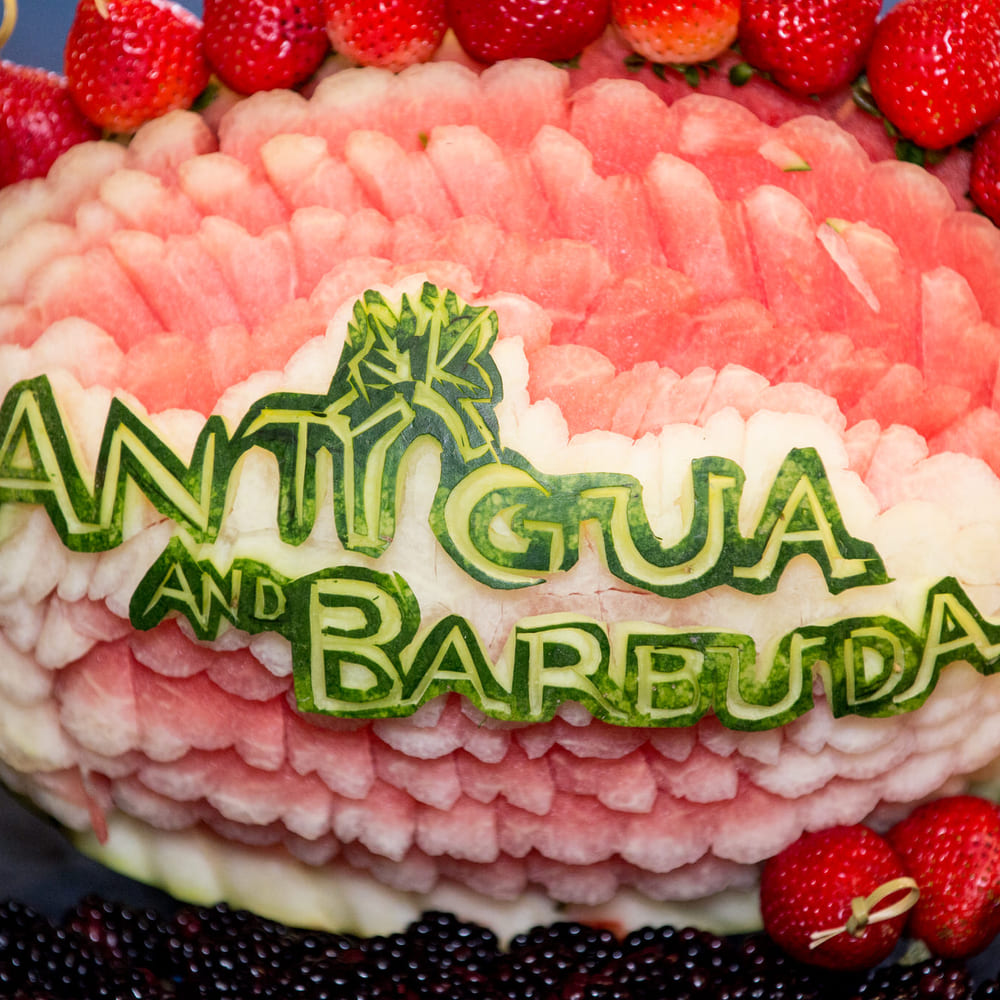 A watermelon carved with Antigua and Barbuda and a palm tree, ringed with strawberries and blackberries.
