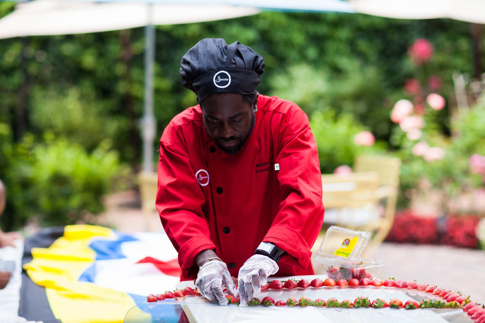 Chef Melvin Myers in a red red chef's coat laying strawberries along a tray at an outdoor event.